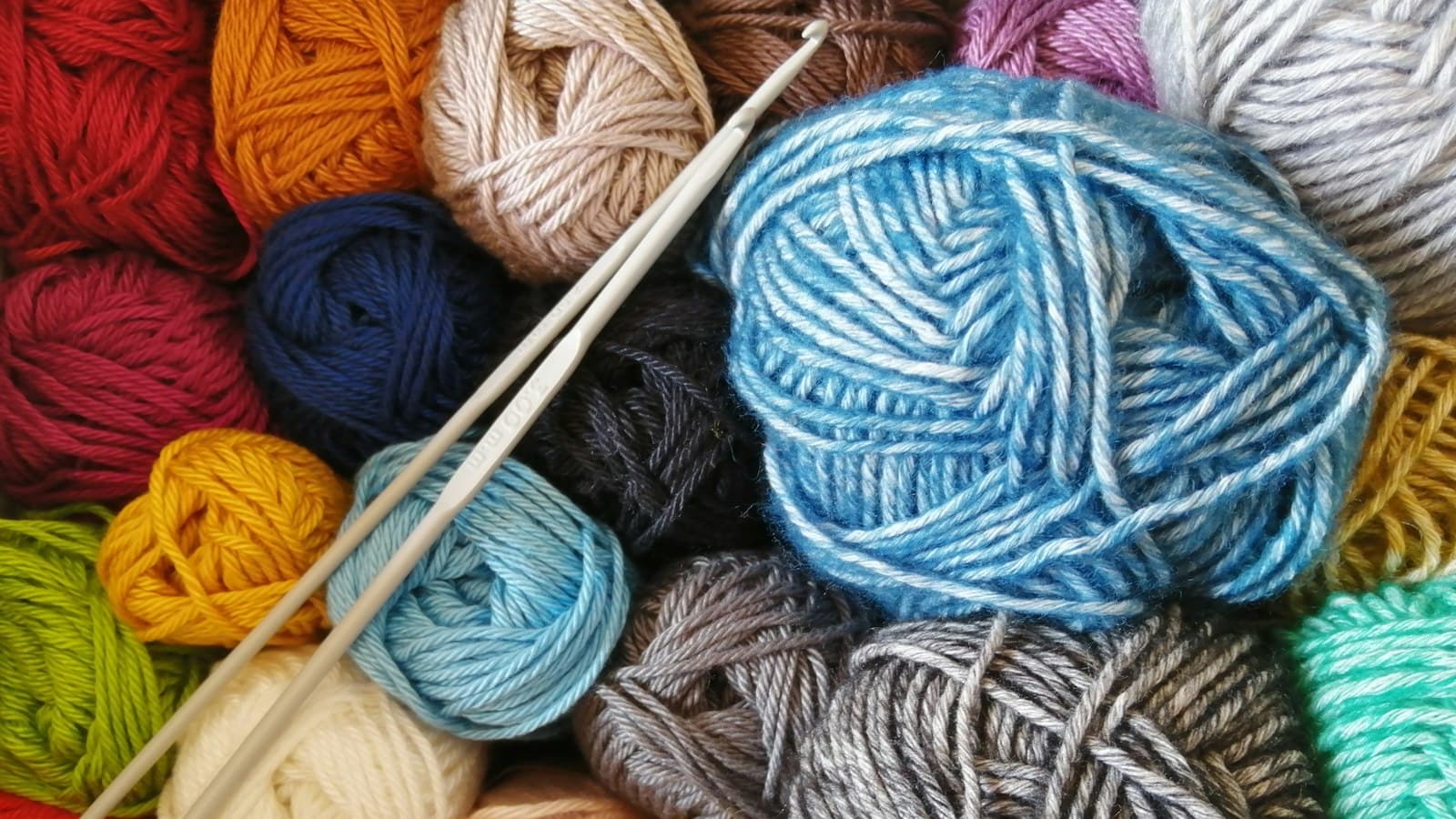 Novelos de lã coloridos e agulhas de tricô sobre uma mesa de trabalho artesanal