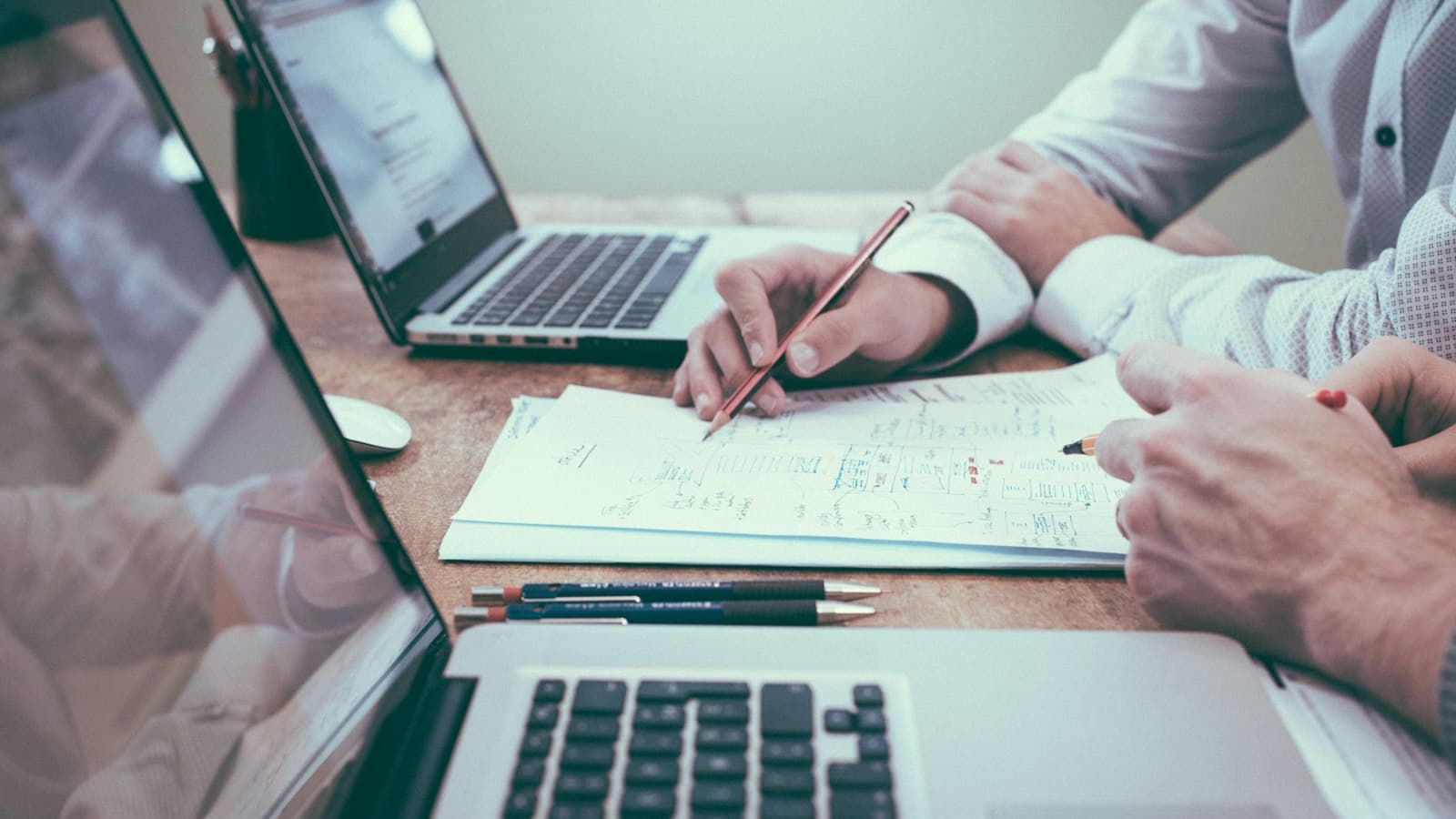 Dois profissionais analisando documentos e planilhas em uma mesa de trabalho